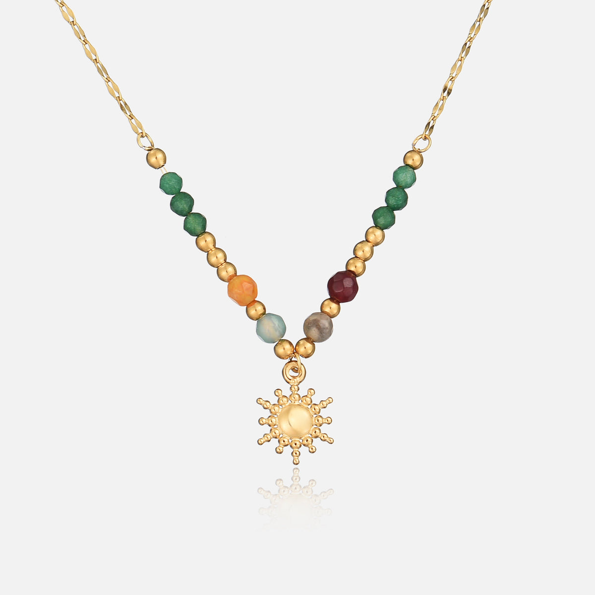 Goldfarbene Kette mit grünen, orangen und roten Perlen und Sonnenanhänger, frontal auf hellem Hintergrund 1