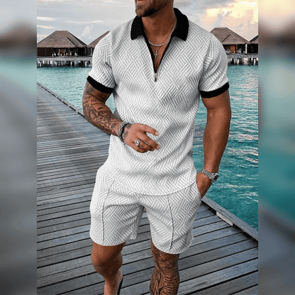 Mann in weißem Sommer-Set mit Muster, schwarzem Kragen, auf Holzsteg am Meer.