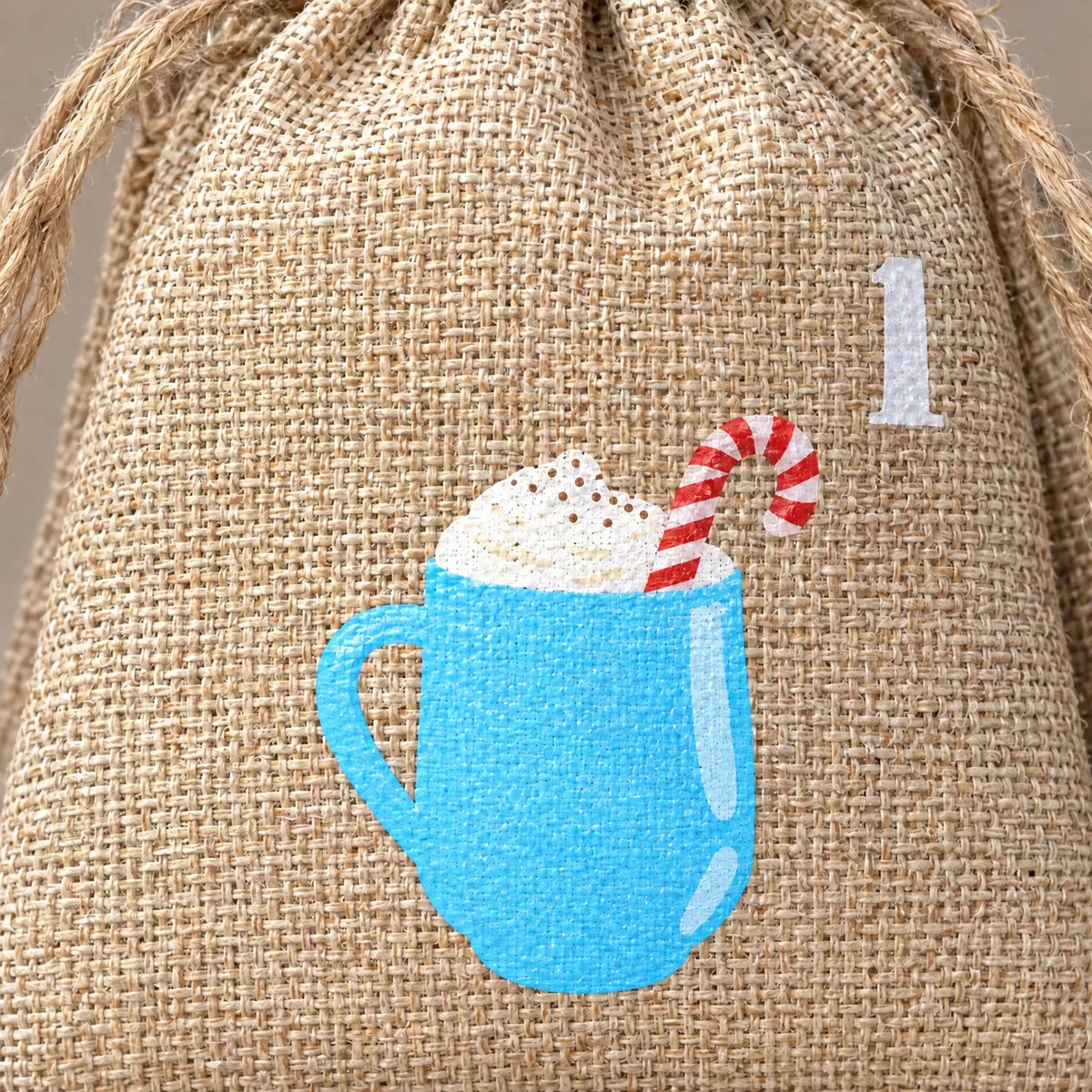 Nahaufnahme eines groben Jutesäckchens mit Kordel, bedruckt mit einer blauen Tasse, Sahnehaube und Zuckerstange sowie der Zahl eins. 3