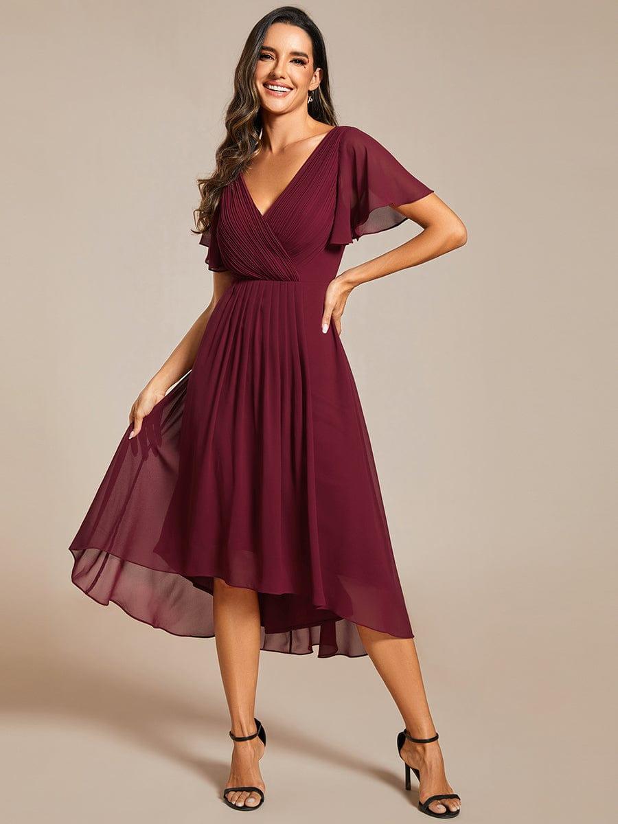 Weinrotes Chiffonkleid frontal, Model hebt mit einer Hand den leichten Rock an, die andere Hand an der Hüfte. 48