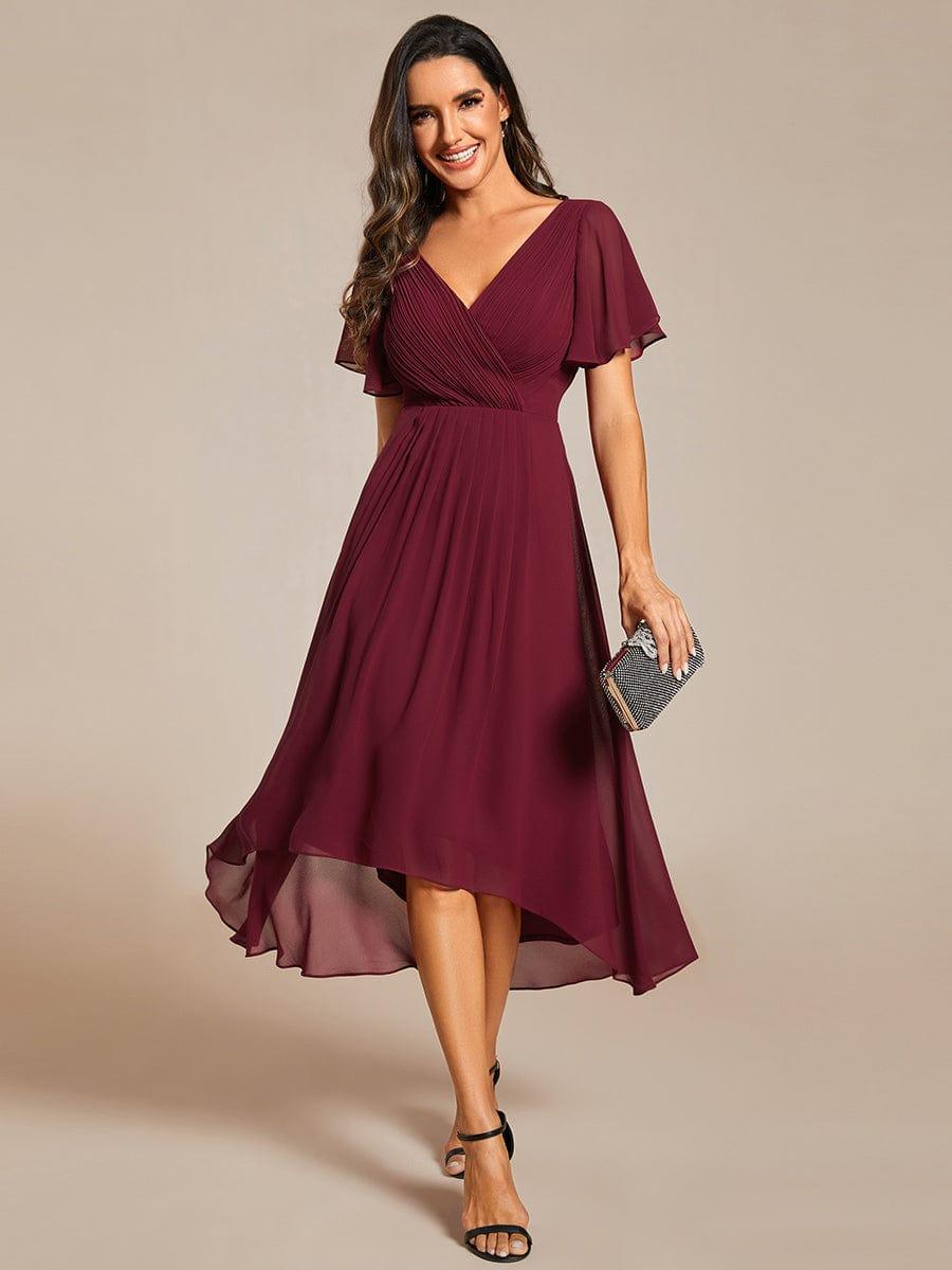 Frontansicht in Burgunderrot: Chiffonkleid mit gewickeltem V-Ausschnitt, Flatterärmeln und asymmetrischem Saum, dazu eine glitzernde Clutch. 3