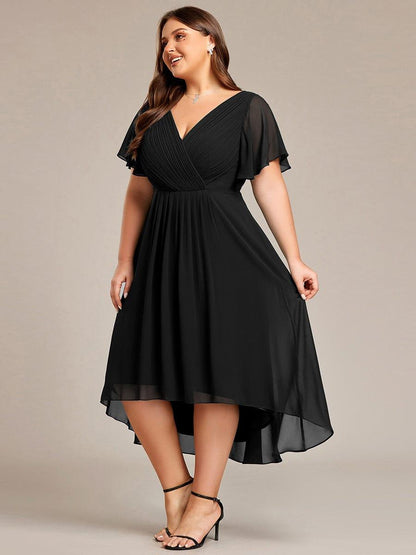 Curvy-Model im schwarzen Kleid, leicht gedreht und lächelnd, Hand am Rock, Vokuhila-Saum fällt weich. 29