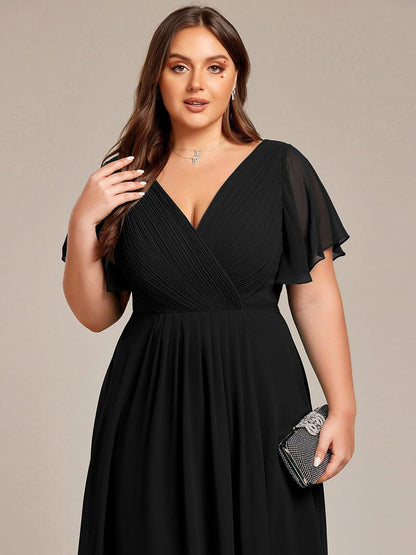 Nahaufnahme des Oberteils am Curvy-Model: schwarzes gerafftes Wickeloberteil, V-Ausschnitt, Flatterärmel, glitzernde Clutch in der Hand. 28