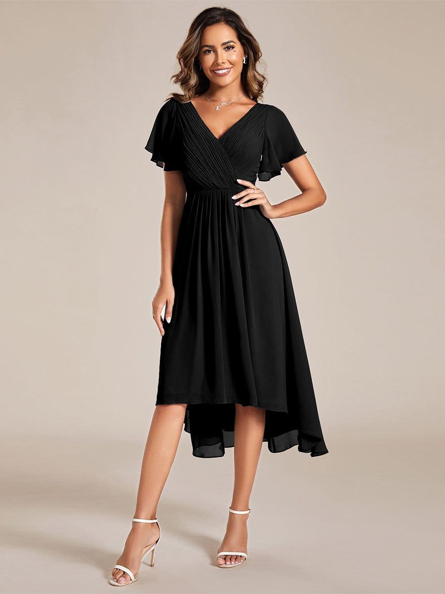 Frau in schwarzem Chiffonkleid mit V-Ausschnitt, Flatterärmeln und Vokuhila-Saum, Frontansicht, eine Hand in die Hüfte gestützt. 21