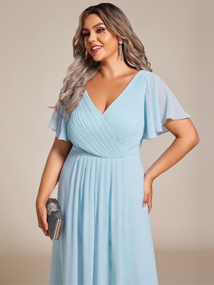 Nahaufnahme des hellblauen Oberteils an einem Plus-Size-Model mit plissiertem V-Ausschnitt, Flatterärmeln und schwarzer Clutch in der Hand. 91