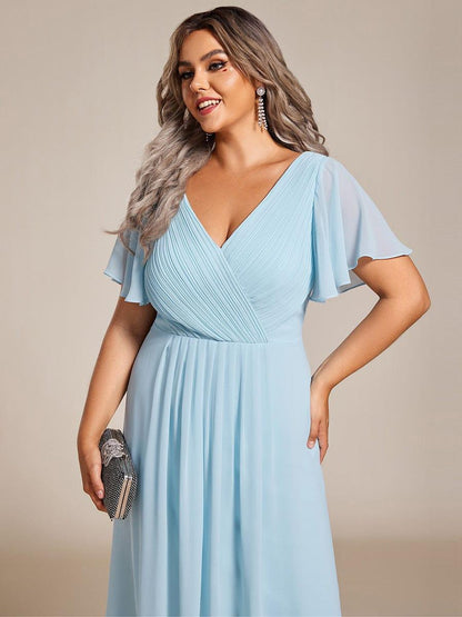 Nahaufnahme des hellblauen Oberteils an einem Plus-Size-Model mit plissiertem V-Ausschnitt, Flatterärmeln und schwarzer Clutch in der Hand. 91