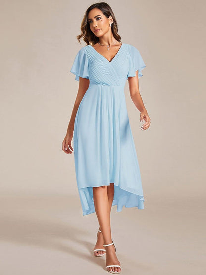 Model in hellblauem Chiffonkleid mit V-Ausschnitt, Flatterärmeln und vorne kürzerem Saum, Frontansicht mit weißen Sandalen. 84