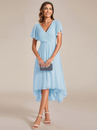 Model in hellblauem Chiffonkleid hält eine dunkle Clutch vor dem Körper, der Saum fällt vorne kürzer als hinten. 87