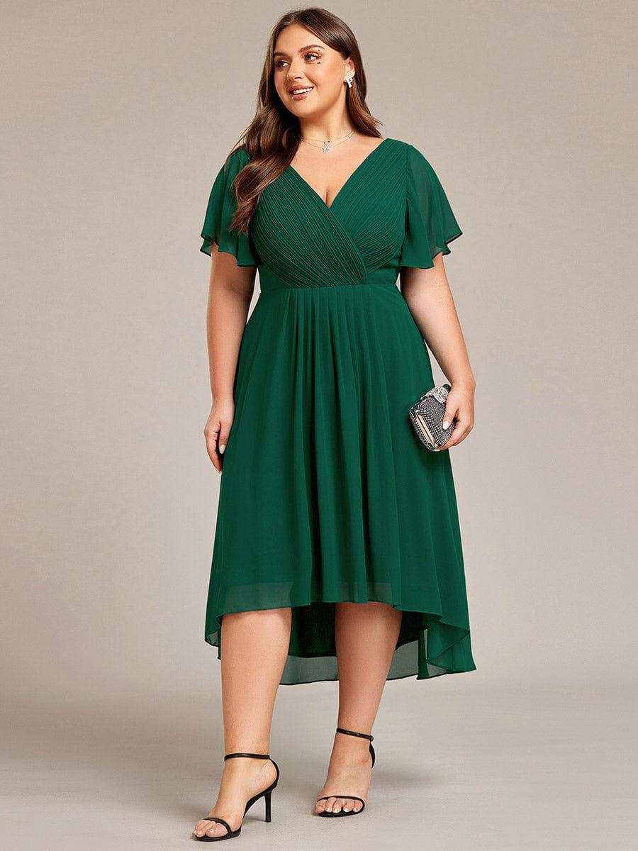 Curvy-Model im dunkelgrünen Kleid in Frontansicht mit kleiner glitzernder Clutch, hoch-tiefer Chiffonsaum. 40