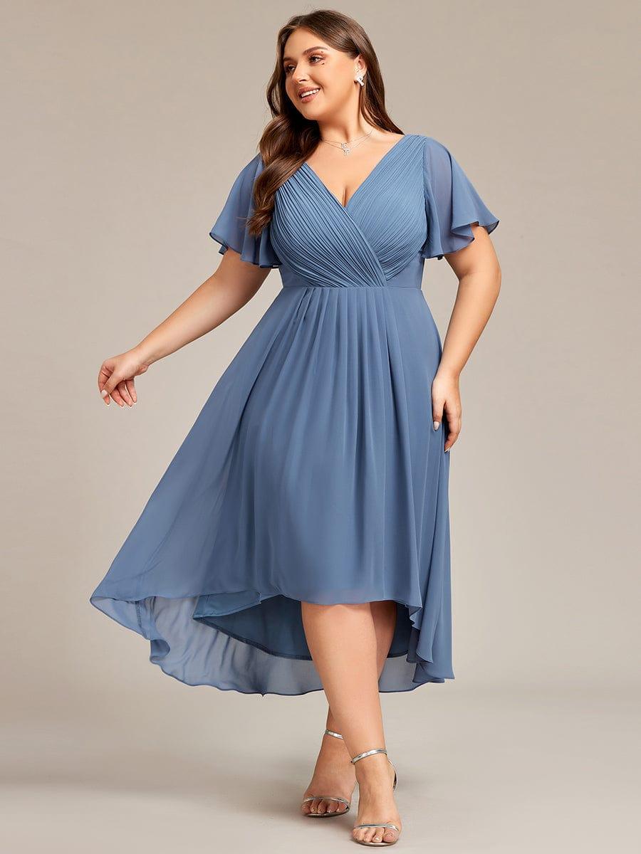 Plus-Size-Model in staubblauem Chiffonkleid mit gerafftem V-Ausschnitt, Flatterärmeln und Vokuhila-Saum, im Schwung fotografiert. 41