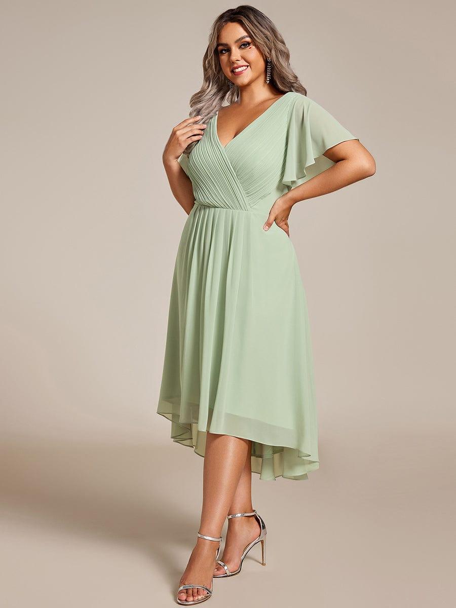 Plus-Size-Model in mintgrünem Chiffonkleid mit gerafftem V-Ausschnitt und Flatterärmeln, dreiviertel von vorn, Hand an der Hüfte, silberne Sandalen. 81
