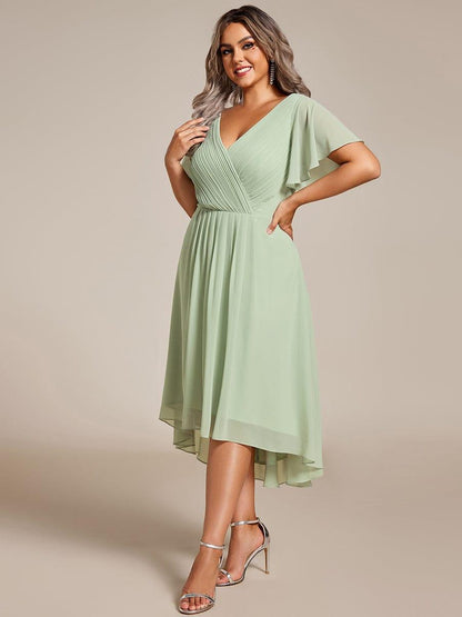 Plus-Size-Model in mintgrünem Chiffonkleid mit gerafftem V-Ausschnitt und Flatterärmeln, dreiviertel von vorn, Hand an der Hüfte, silberne Sandalen. 81