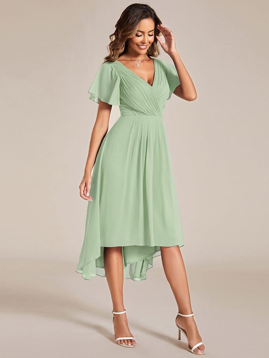 Salbeigrünes Kleid mit Flatterärmeln und asymmetrischem Saum in seitlicher Ganzkörperansicht, Model mit Hand am Kopf. 80