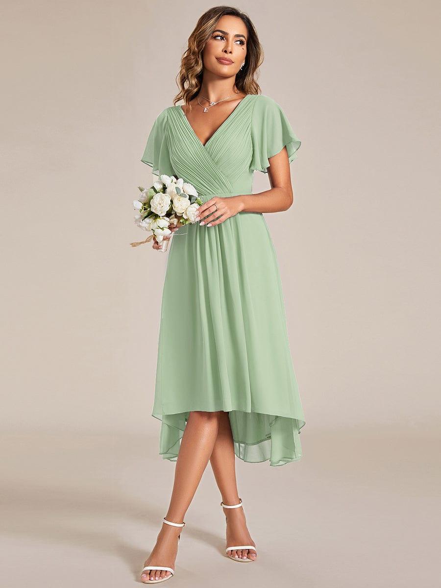Model in salbeigrünem Kleid hält einen Strauß weißer Blumen, Blick zur Seite, Chiffonsaum mit Vokuhila-Schnitt. 79