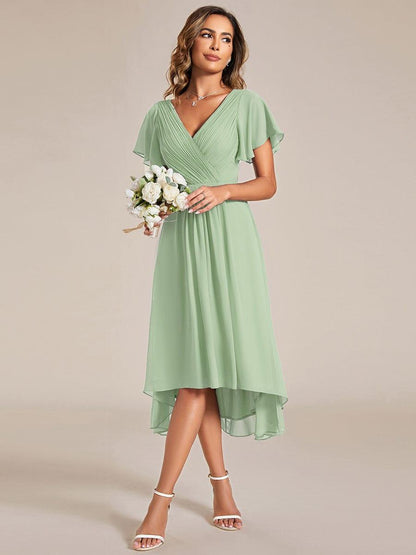 Model in salbeigrünem Kleid hält einen Strauß weißer Blumen, Blick zur Seite, Chiffonsaum mit Vokuhila-Schnitt. 79