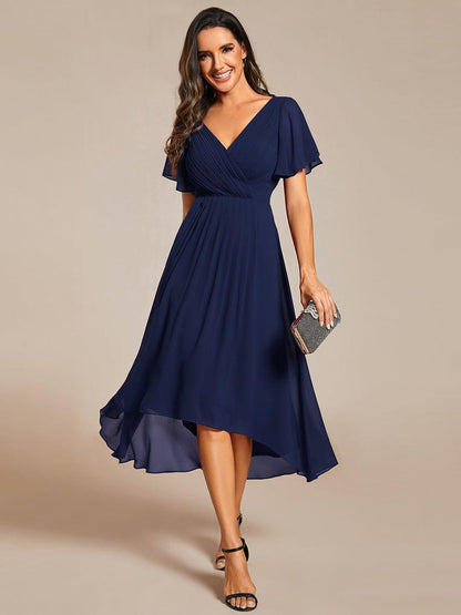 Frontansicht in Marineblau: Chiffonkleid mit gerafftem V-Ausschnitt und Flatterärmeln, getragen mit schwarzen Sandalen und glitzernder Clutch. 1