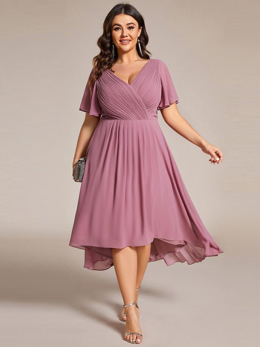 Mauvefarbenes Kleid mit asymmetrischem Saum an einem Plus-Size-Model von vorn, dazu silberne Sandaletten und eine glitzernde Clutch. 63