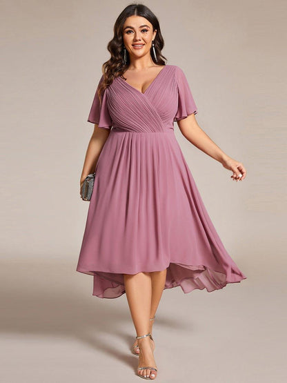 Mauvefarbenes Kleid mit asymmetrischem Saum an einem Plus-Size-Model von vorn, dazu silberne Sandaletten und eine glitzernde Clutch. 63