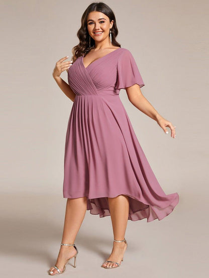 Plus-Size-Model in leichter Drehung im mauvefarbenen Kleid, der asymmetrische Chiffonsaum schwingt dabei sichtbar mit. 67
