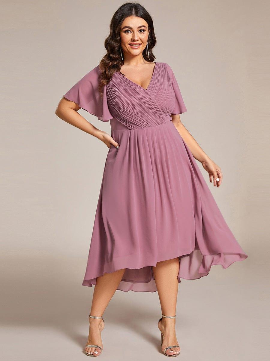Plus-Size-Model in mauvefarbenem Chiffonkleid mit Hand in der Hüfte, hoch-tiefer Saum und goldfarbene Sandaletten. 66