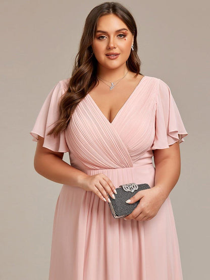 Nahaufnahme des rosa Oberteils: gerafftes Wickeldesign mit V-Ausschnitt und Flatterärmeln, Model hält eine glitzernde Clutch. 33