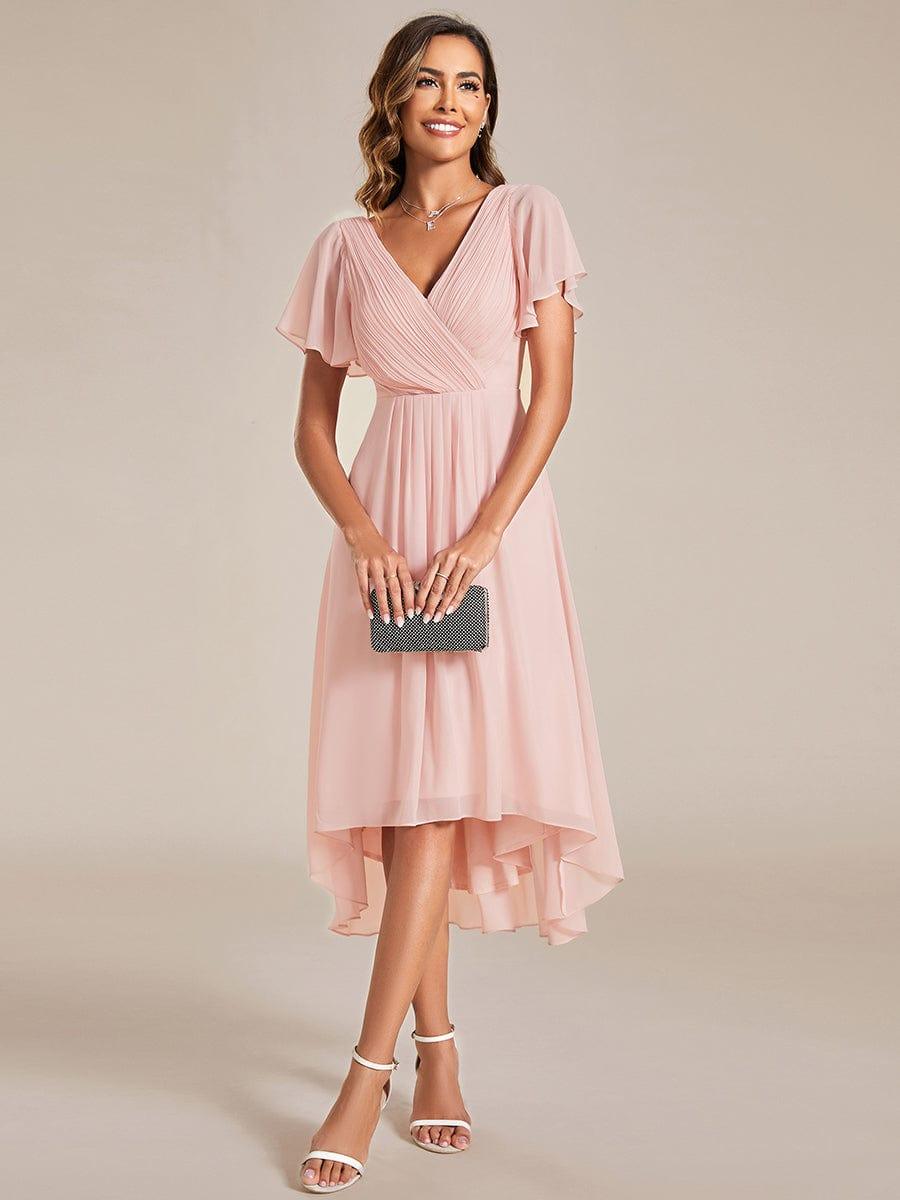 Frontansicht in Rosé: Model hält eine schwarze Clutch vor dem Körper, Kleid mit V-Ausschnitt, Flatterärmeln und Vokuhila-Saum. 15