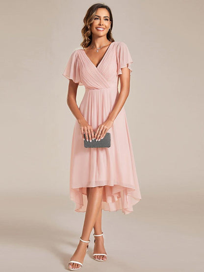 Frontansicht in Rosé: Model hält eine schwarze Clutch vor dem Körper, Kleid mit V-Ausschnitt, Flatterärmeln und Vokuhila-Saum. 15