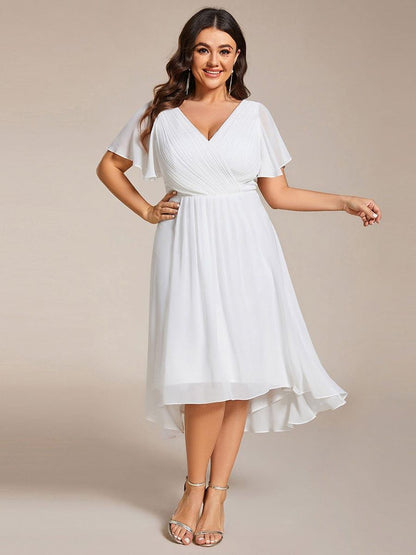 Plus-Size-Model im weißen Kleid mit Flatterärmeln und asymmetrischem Saum, eine Hand in der Hüfte, silberne Sandaletten. 73