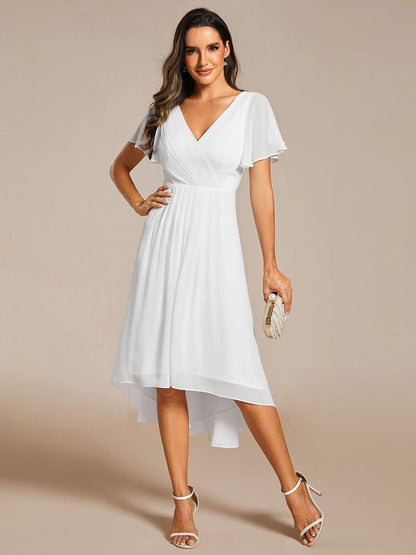 Weißes Kleid mit Vokuhila-Saum in Ganzkörperansicht, Model mit Hand in der Hüfte und Perlenclutch in der anderen Hand. 71