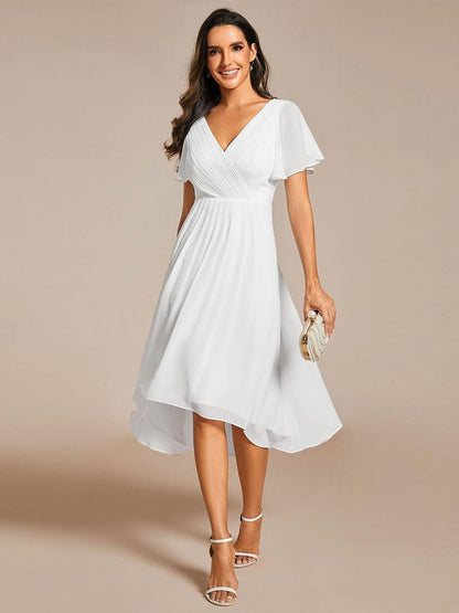 Weißes Chiffonkleid mit V-Ausschnitt und Flatterärmeln von vorn, Model hält eine Perlenclutch und trägt weiße Sandaletten. 68