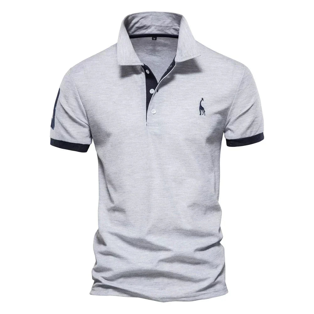 Hellgraues Poloshirt in der Frontansicht mit dunkelblauen Bündchen, dunkler Knopfleiste und Giraffenstickerei sowie Aufnäher 4