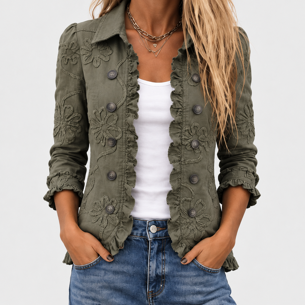 Nahaufnahme des Oberkörpers: olivgrüne Jacke mit Blumenstickerei, Rüschenkante und dunklen Knöpfen, offen über weißem Top und Jeans getragen. 1