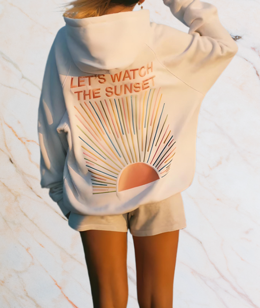 Frau in weißem Hoodie mit Sonnenuntergangsdesign und Schriftzug "Let's Watch the Sunset".