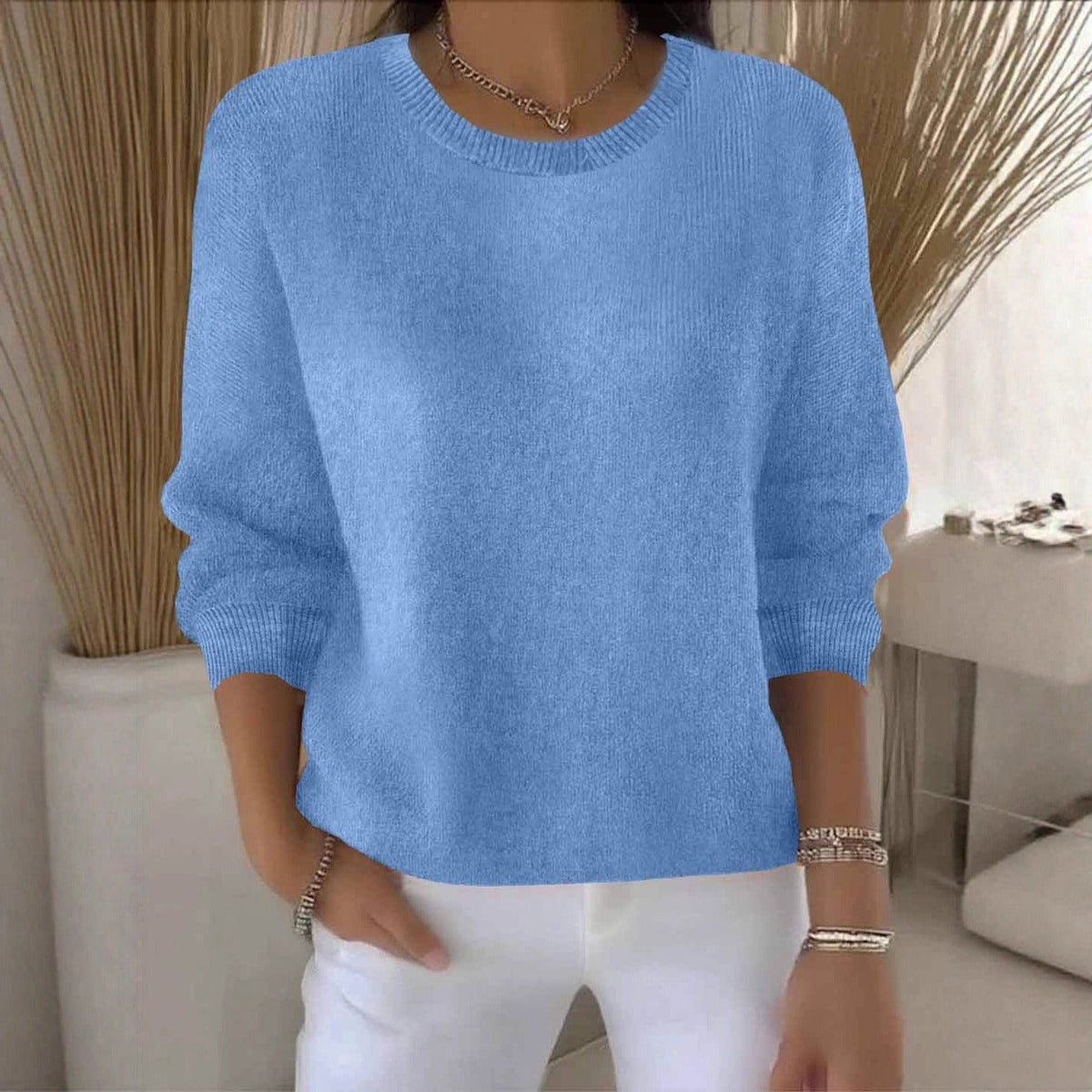 Frontansicht des hellblauen Strickpullovers mit Rundhalsausschnitt, getragen zu weißer Hose vor Dekogräsern 13