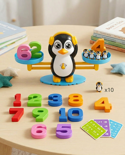 Pinguin-Waage auf rundem Holztisch mit verstreuten Zahlenblöcken, Aufgabenkarten und einer Pinguinfigur mit Hinweis auf zehn 9