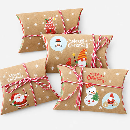 Vier Kraftpapier-Kissenboxen mit rot-weißer Kordel und verschiedenen Weihnachtsmotiven wie Wichtel, Schneemann und Weihnachtsmann auf hellem Hintergrund. 2
