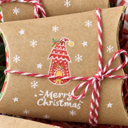 Nahaufnahme einer Kissenbox aus Kraftpapier mit rot-weißer Kordel, Schleife, Schneeflocken und einem roten Häuschen als Weihnachtsmotiv. 3
