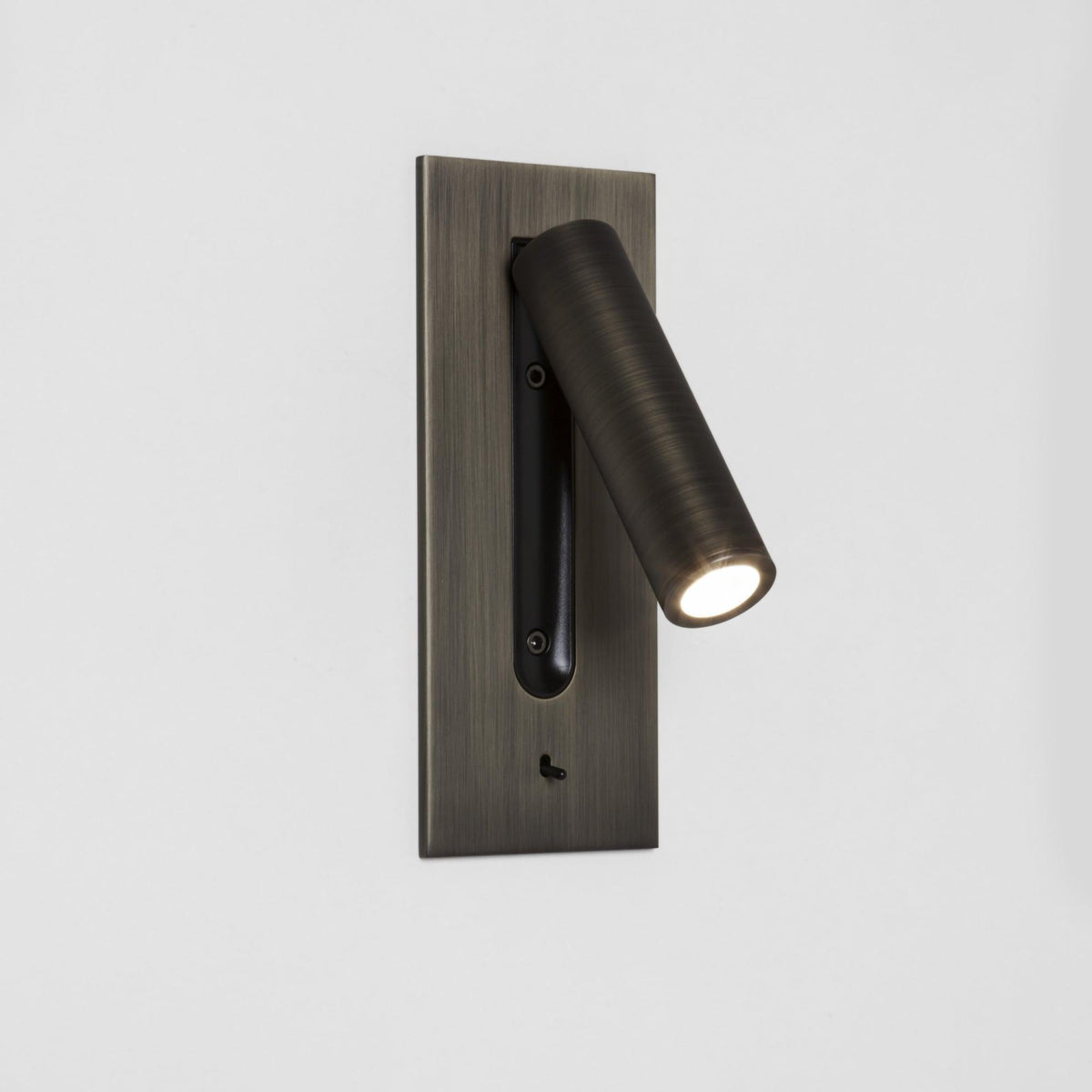 Bronzefarbene Wandleuchte mit eingeschaltetem Strahler, der schräg nach rechts unten leuchtet, an weißer Wand 17