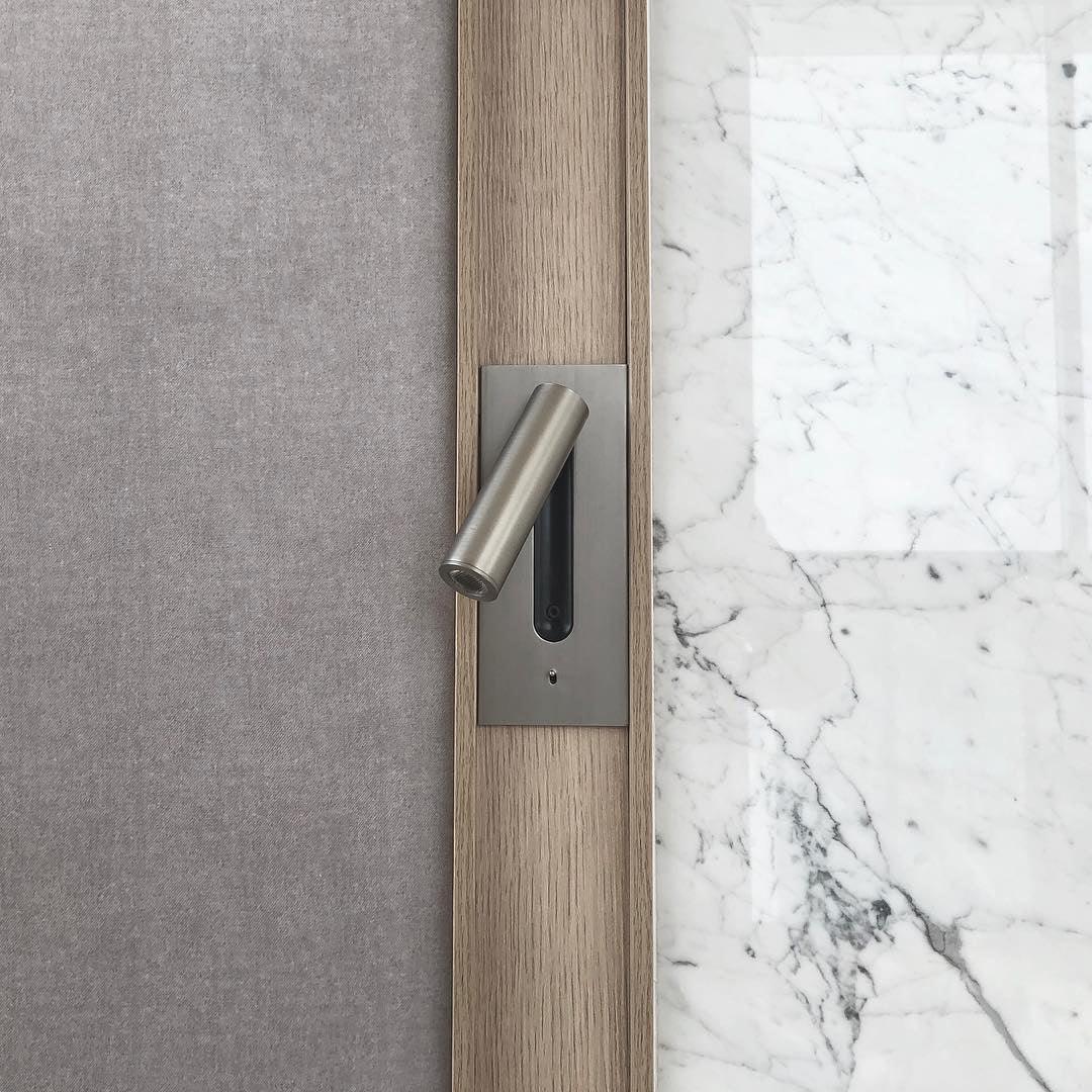 Detailaufnahme einer Wandleuchte in mattem Nickel, eingefasst in Eichenholz neben Stoffwand und weißem Marmor 33