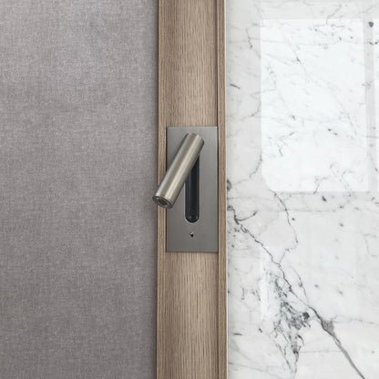 Detailaufnahme einer Wandleuchte in mattem Nickel, eingefasst in Eichenholz neben Stoffwand und weißem Marmor 33