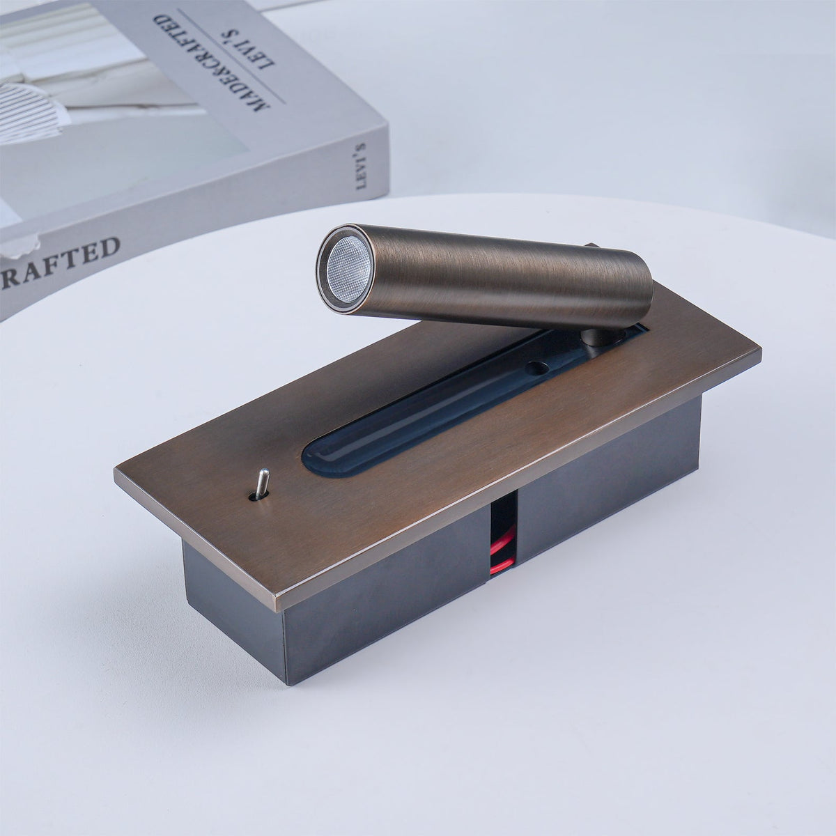 Wandleuchte in Bronze liegend auf einem weißen Tisch, Rückgehäuse und Kabel sichtbar, daneben ein Buch 13
