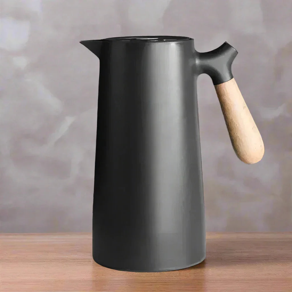 Schwarze nordische Thermoskanne mit Holzgriff auf Holztisch vor grauem Hintergrund.