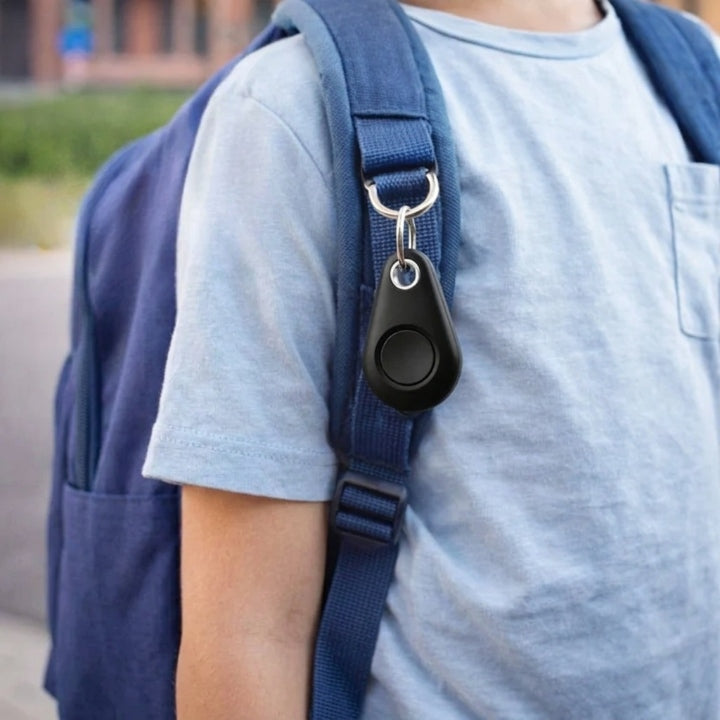 Schwarzer Tracker mit Ring am Schulterriemen eines blauen Rucksacks, Nahaufnahme an einem Kind im hellblauen T-Shirt 3