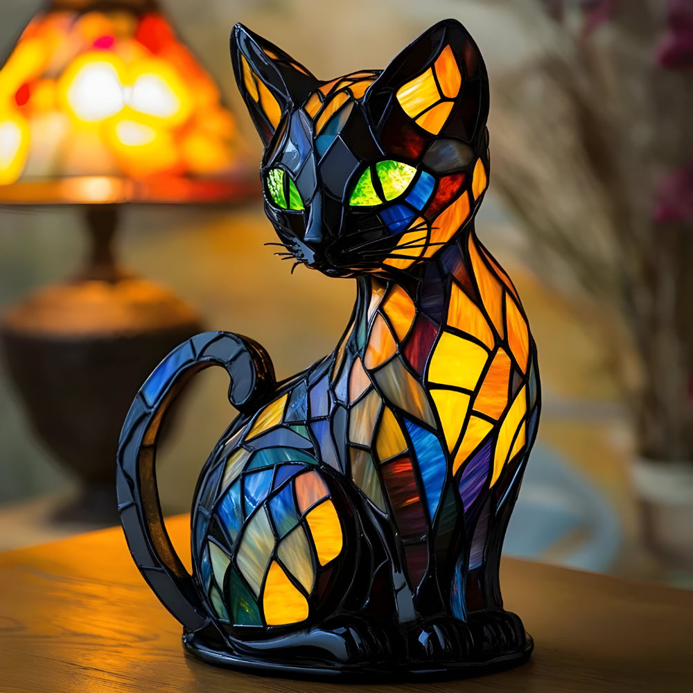 Sitzende schwarze Katzenfigur mit bunten Glasmosaik-Flächen und grünen Augen auf einem Holztisch vor einer leuchtenden Lampe 1