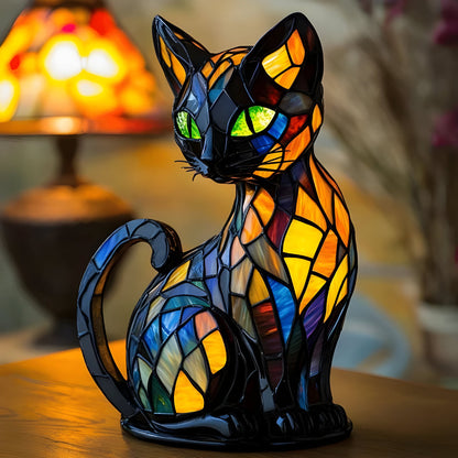 Sitzende schwarze Katzenfigur mit bunten Glasmosaik-Flächen und grünen Augen auf einem Holztisch vor einer leuchtenden Lampe 1
