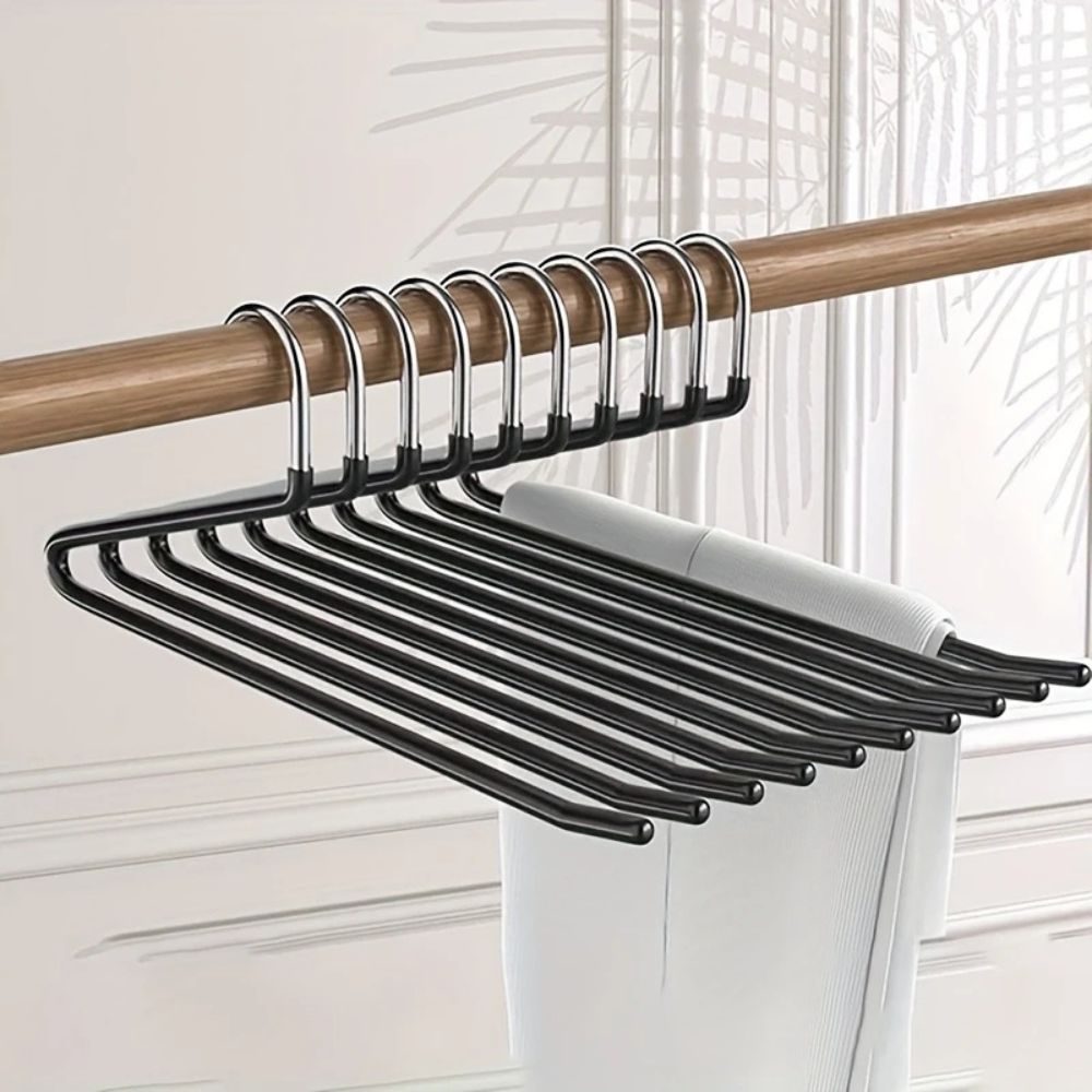 Mehrere schwarze Hosenbügel hängen dicht an einer Holzstange, über einem Bügel liegt eine helle Hose 1