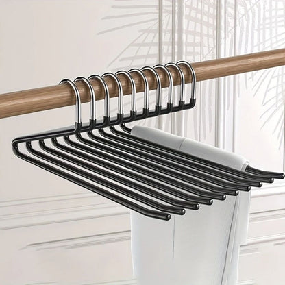 Mehrere schwarze Hosenbügel hängen dicht an einer Holzstange, über einem Bügel liegt eine helle Hose 1