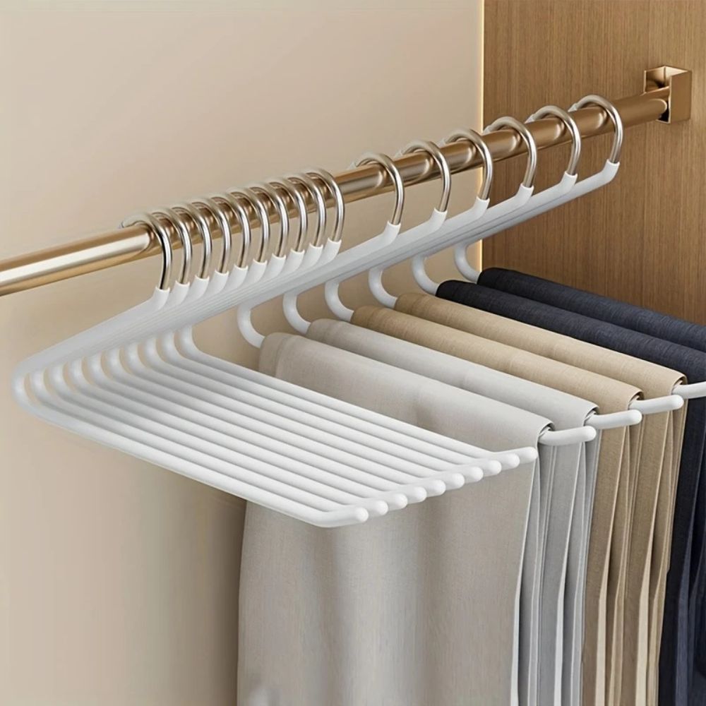 Weiße Hosenbügel an einer Kleiderstange im Schrank, behängt mit Hosen in Beige, Grau und Dunkelblau 3