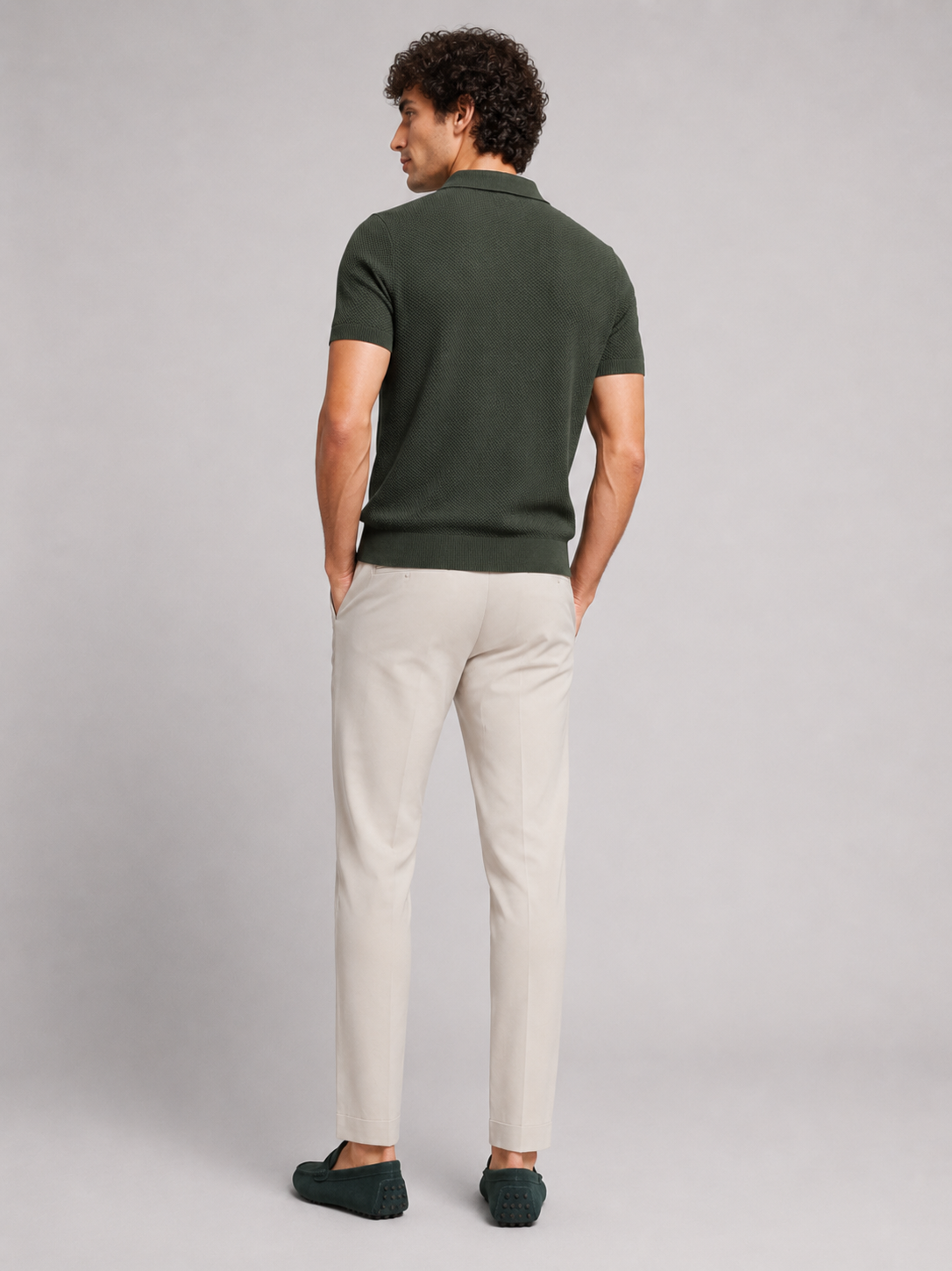 Rückansicht des dunkelgrünen Poloshirts am Model, mit heller Hose und dunkelgrünen Mokassins, Blick über die Schulter 14