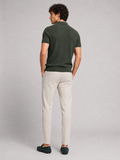 Rückansicht des dunkelgrünen Poloshirts am Model, mit heller Hose und dunkelgrünen Mokassins, Blick über die Schulter 14